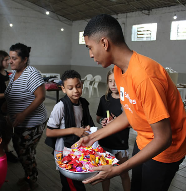 Imagem de um integrante voluntário d o instituto AM dist ribuindo doces para crianças em um abrigo.