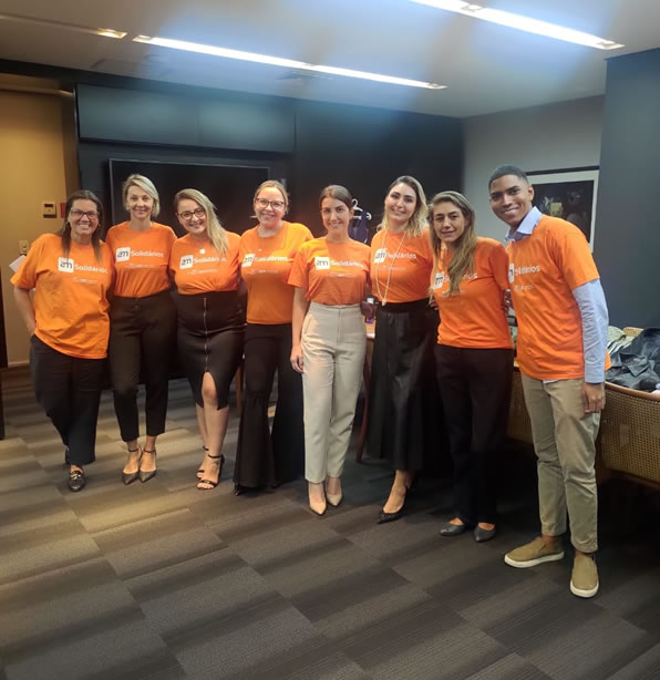 Imagem de 8 integrantes voluntário do Instituto AM com camisetas laranjas abraçados.