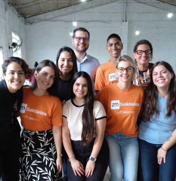 Imagem de alguns integrantes voluntário do Instituto AM com camisetas laranjas abraçados em um abrigo de Porto Alegre.