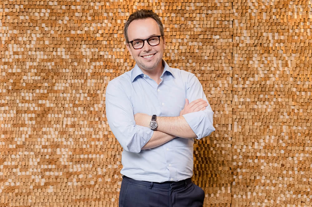 Imagem do sócio fundador Fabio Goldschmidt sorrindo, um homem branco de óculos, camisa social clara e calça preta.